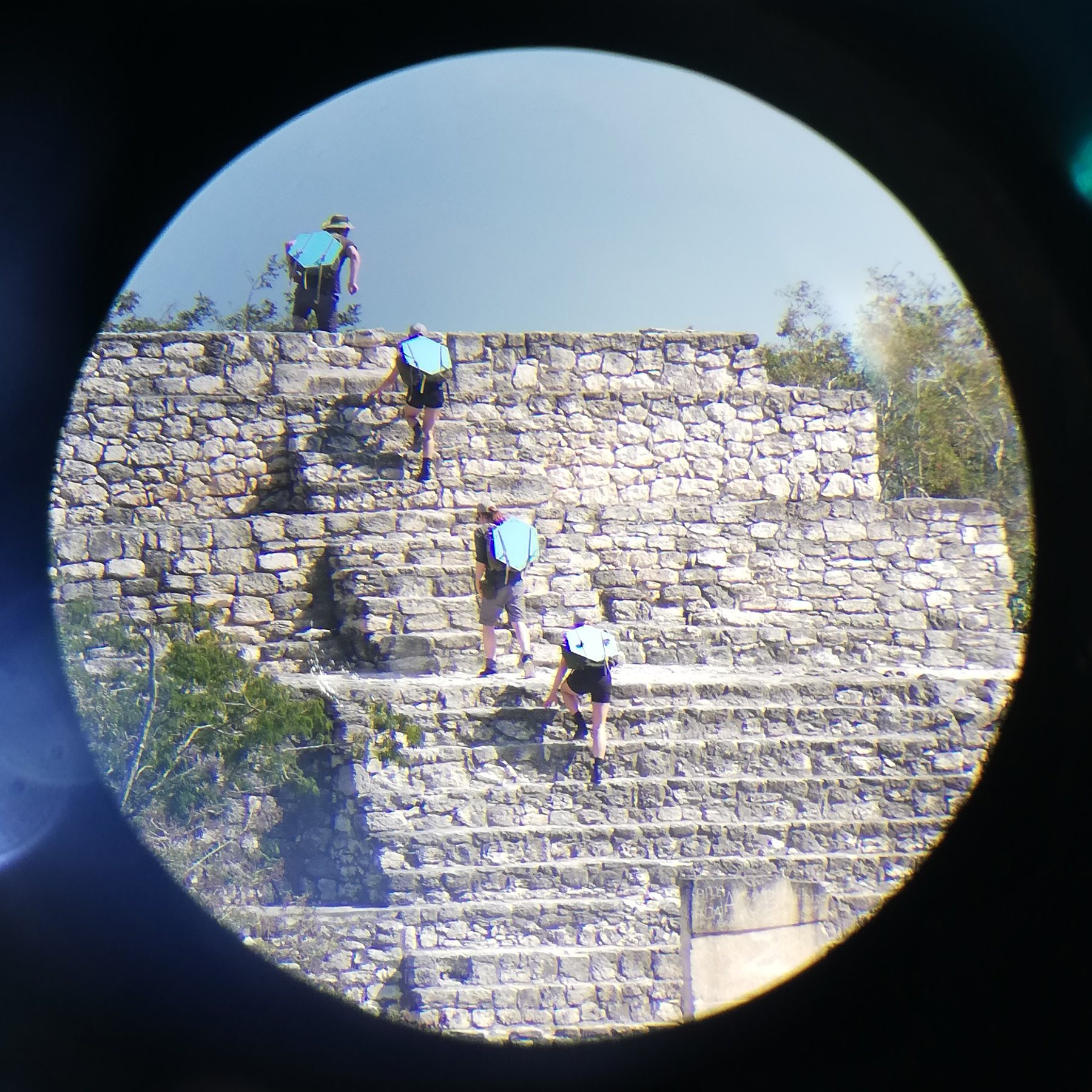 Two figures scaling ancient stone ruins, seen through a circular scope, Calakmul