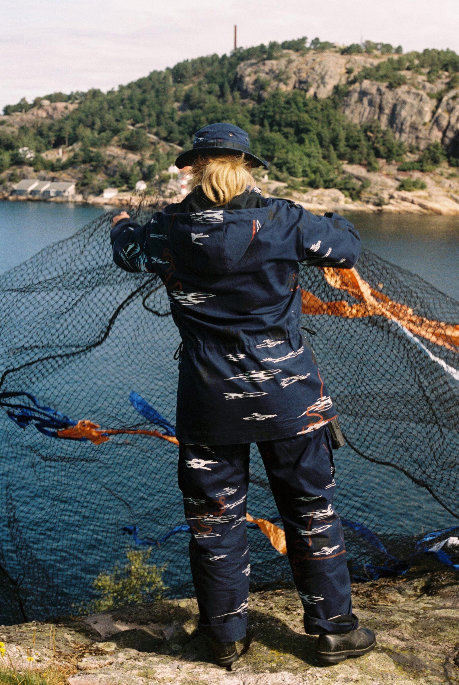 Figure in printed navy uniform holding a fishing net at the shoreline