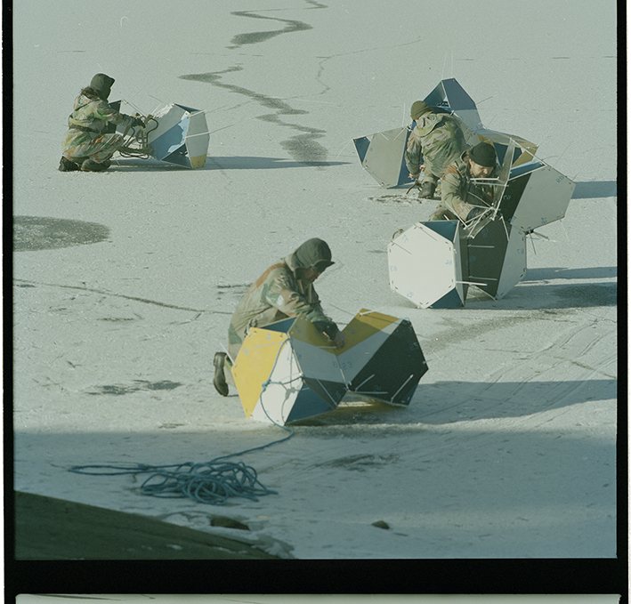 Two figures assembling a hexagonal panel structure in snow, Isesjø